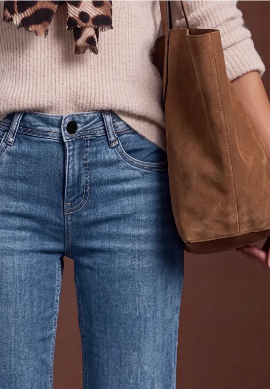 Femme en pull beige, écharpe léopard, jean bleu et sac en cuir marron.