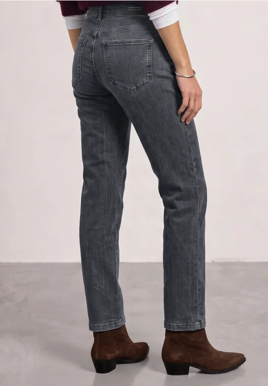 Person trägt graue gerade geschnittene Jeans und braune Ankle-Boots vor neutralem Hintergrund.