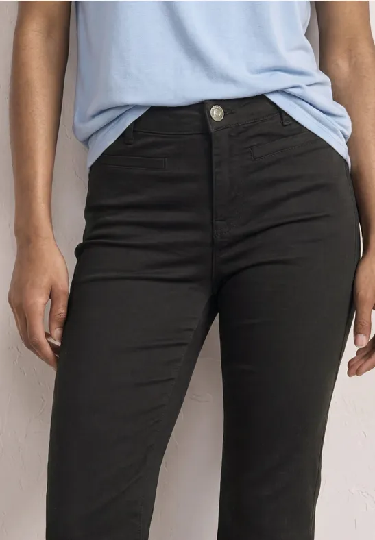 Close-up van iemand met zwarte, taillehoge spijkerbroek en lichtblauw shirt.