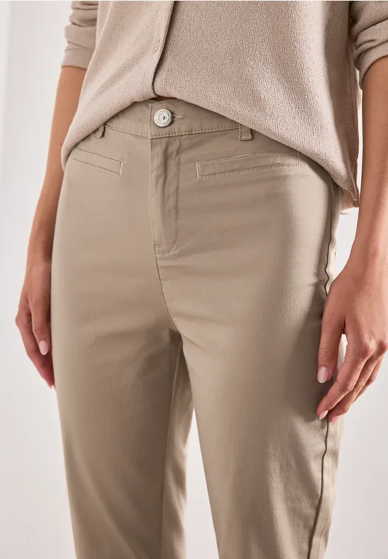 Close-up van een persoon met beige chino's, zijzakken en een lichtgekleurde trui.