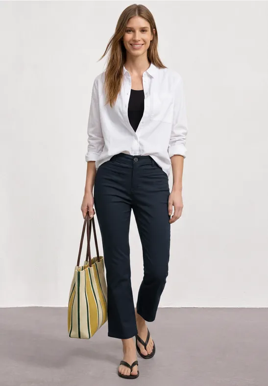 Frau trägt weiße Bluse, schwarzes Top, dunkle Hose, Flip-Flops und gestreifte Handtasche.