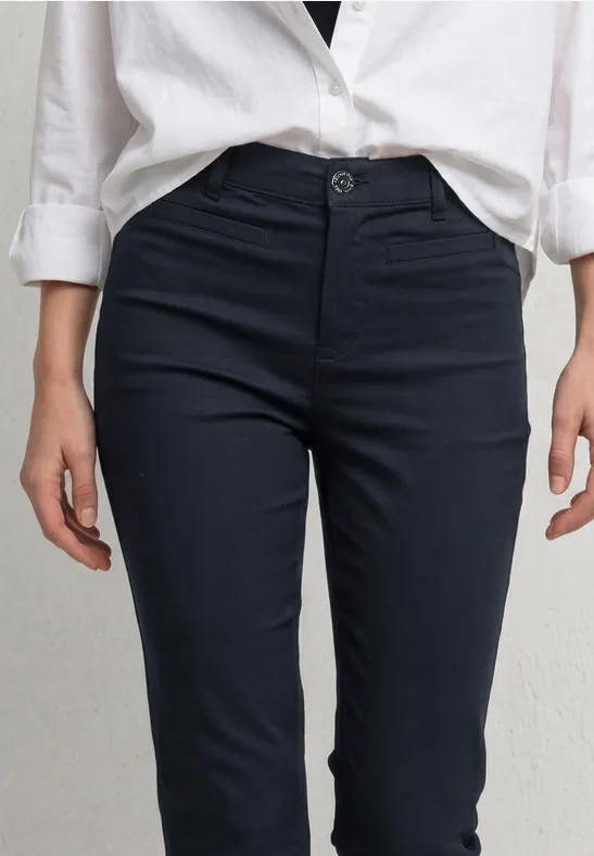Eine Person trägt ein weißes Hemd und dunkle, schmale Chino-Hose.
