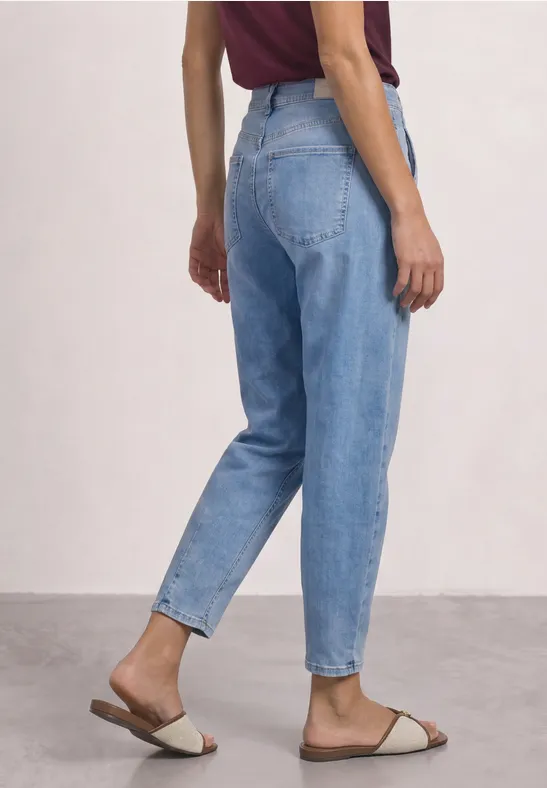 Frau trägt hochgeschnittene, hellblaue Jeans mit schmal zulaufendem Bein und cremefarbene Pantoletten.