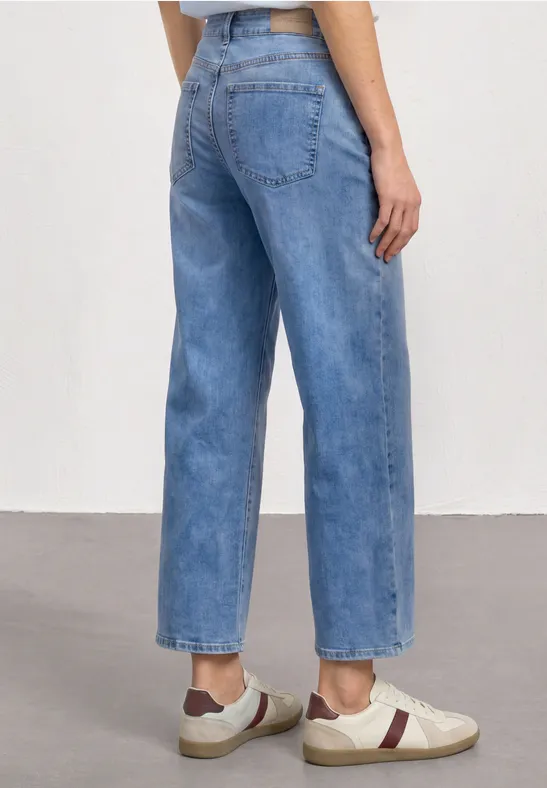Person trägt gerade geschnittene hellblaue Jeans und weiße Sneaker mit roten Details, Rückansicht.