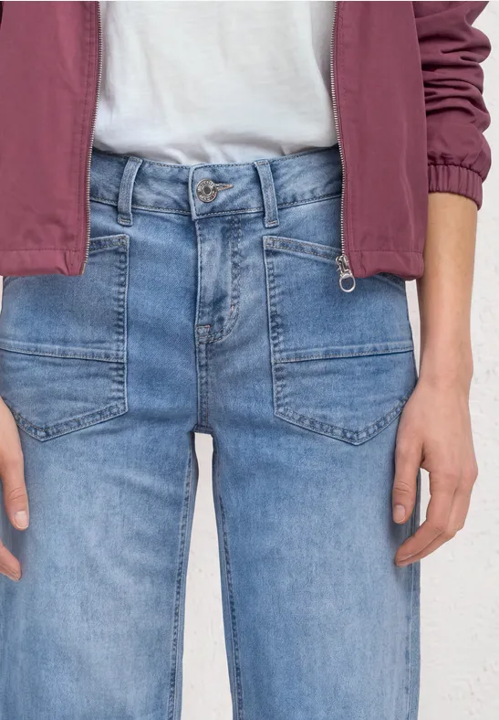 Person trägt helle Jeans, weißes Shirt und rote Jacke, nur Oberkörper und Hände sichtbar.