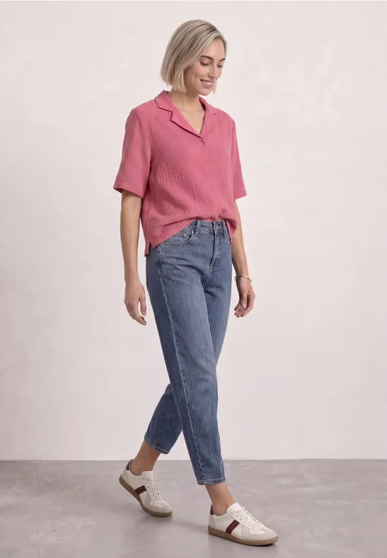 Vrouw draagt roze top, blauwe jeans en witte schoenen tegen een lichte achtergrond
