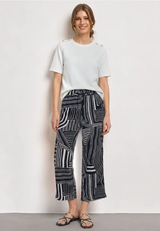 Vrouw met een wit T-shirt en zwarte, wijdvallende broek met patronen en sandalen