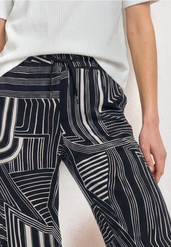Persoon draagt een wit truitje en een zwart-witte broek met abstract streepdessin.