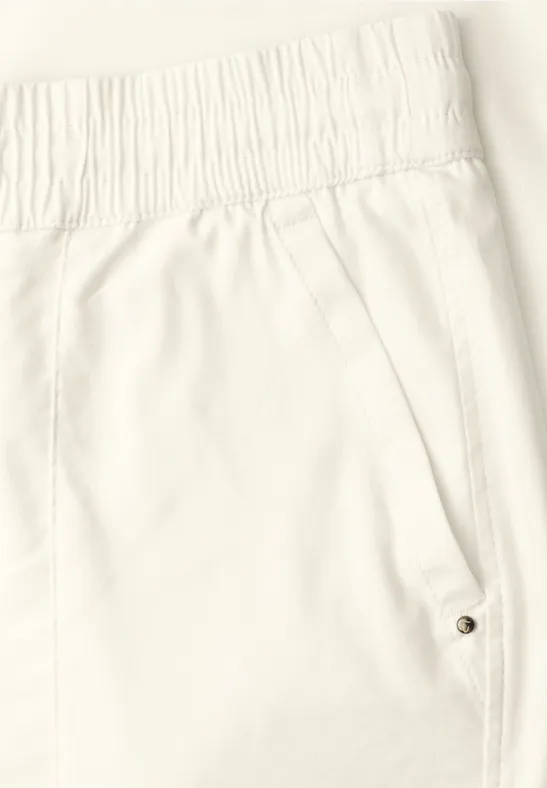 Close-up van een witte broek met elastische taille en zijzak met drukknoop.