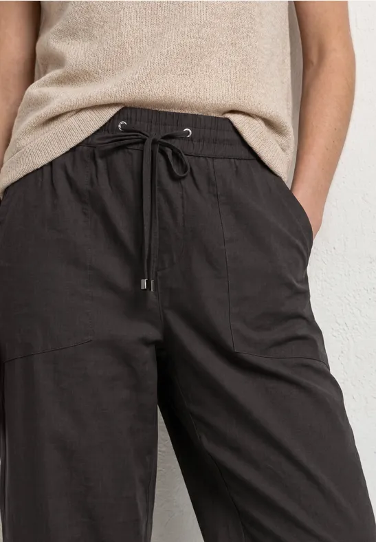 Schlichte schwarze Leinenhose mit Tunnelzug und beige Top, Hände locker in den Taschen