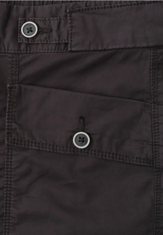 Detailaufnahme eines dunklen Kleidungsstücks mit zwei Knöpfen und einer aufgesetzten Tasche.