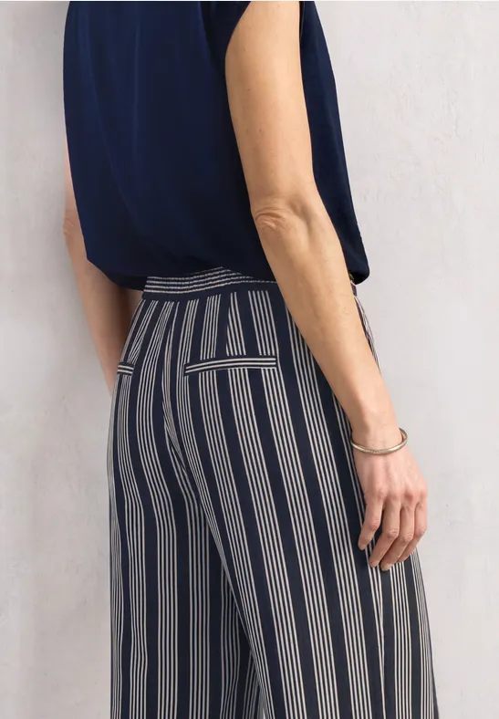 Frau trägt marineblaues Top und hoch taillierte, grau-blaue Hose mit vertikalen Streifen, seitliche Ansicht.