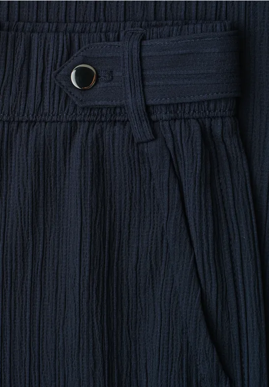 Detailaufnahme eines dunkelblauen, plissierten Stoffs mit Bund, Gürtelschlaufe und Druckknopf.