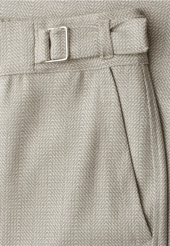 Nahaufnahme einer beigefarbenen Hose aus Fischgrätenstoff mit seitlicher Riemenverstellung und Tasche