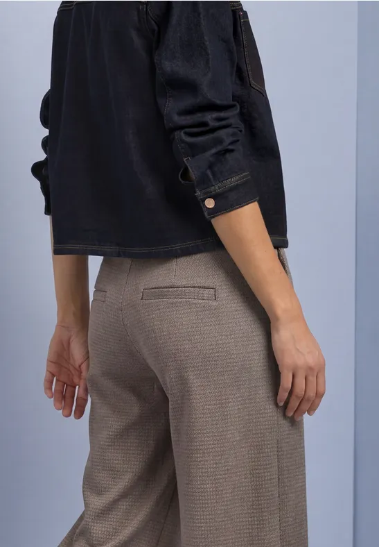 Person von der Taille abwärts in graubrauner Hose mit Leistentasche und schwarzer Bluse, seitlich von hinten.