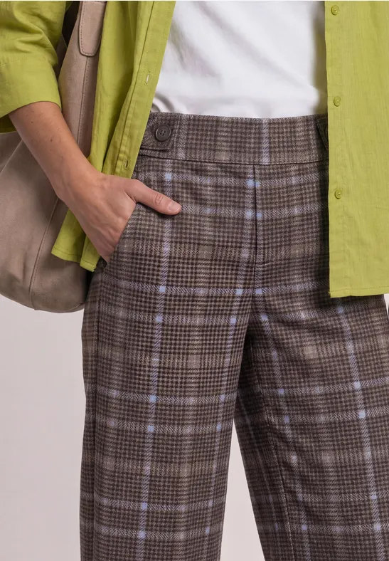 Person trägt karierte braune Hose, weißes Top, grünes Hemd und eine Schultertasche.