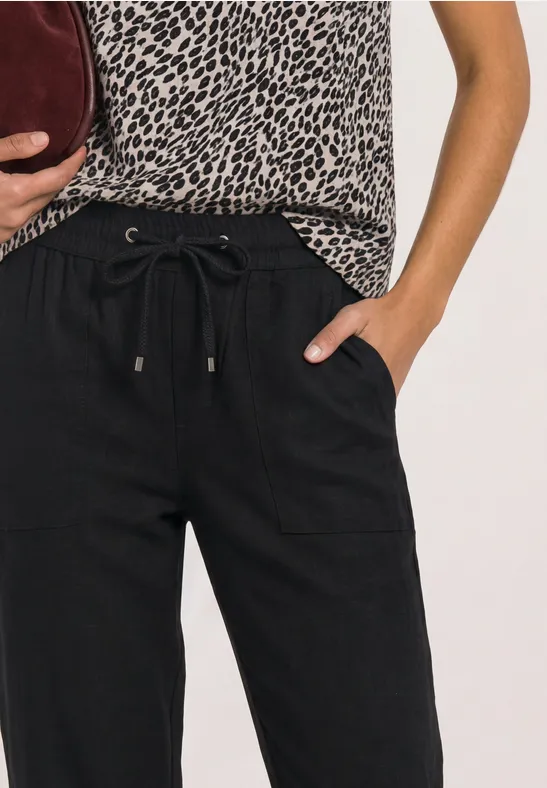Vrouw met zwarte broek met koord, luipaardtop en bordeaux clutch.