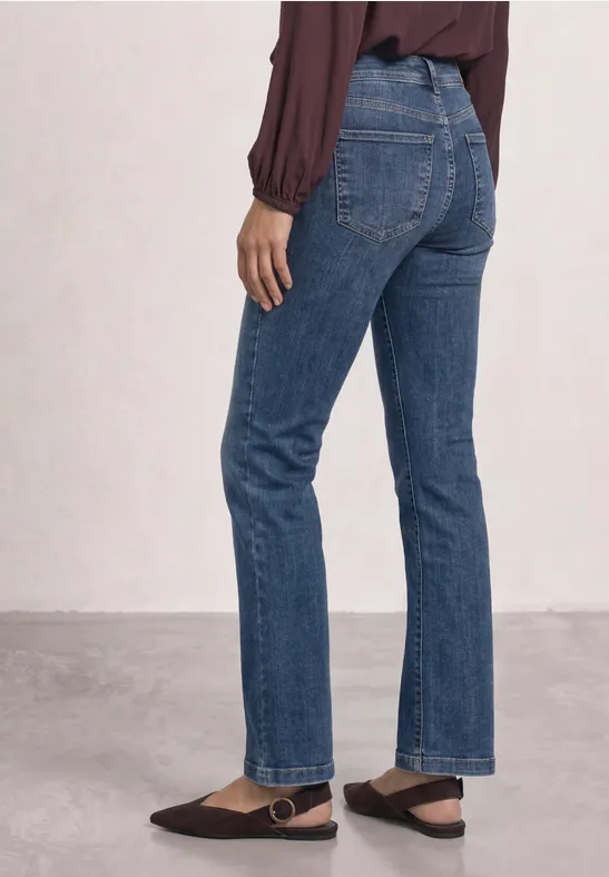 Eine Person trägt gerade geschnittene blaue Jeans und eine burgunderrote Bluse.
