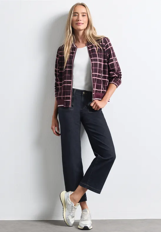 Frau mit Karo-Jacke, weißem Top, weiter Jeanshose und weißen Sneakern.