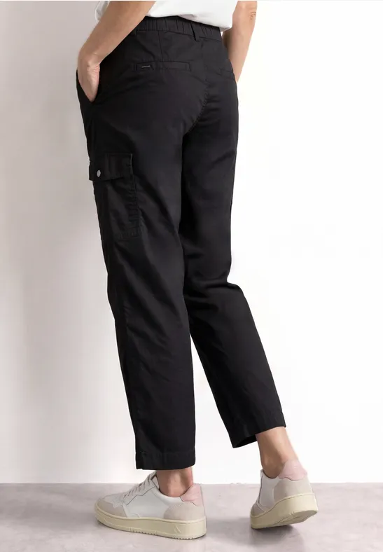 Schlichter schwarzer Cargo-Hose im 7/8-Stil mit seitlichen Taschen, kombiniert mit weißen Sneakern.