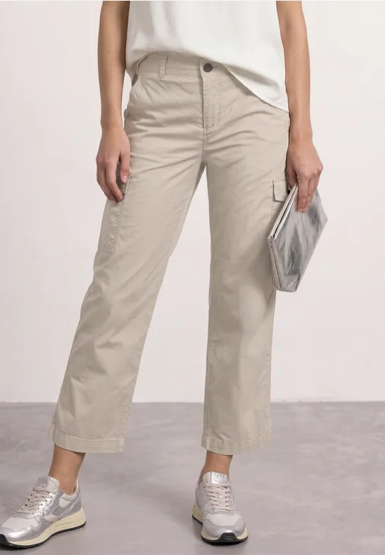 Beine in beigen Culotte-Hosen, weißem Top, silbernen Sneakern und silberner Clutch