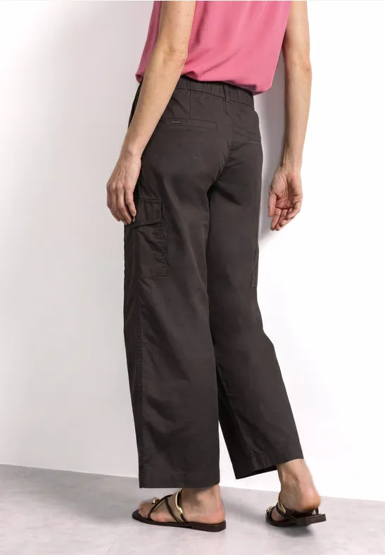 Rugbeeld van persoon met wijde, donkere broek, roze top en bruine sandalen.