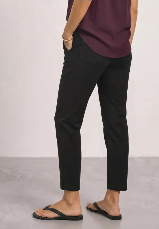 Eine Person trägt eine violette Bluse, schwarze Capri-Hose und schwarze Flip-Flops.