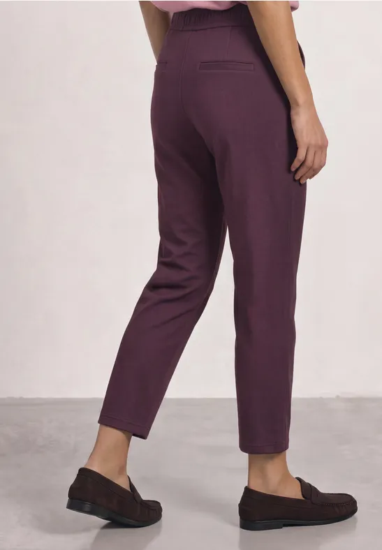 Eine Person steht seitlich, trägt violette Hose und schwarze Hausschuhe.