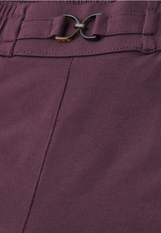 Nahaufnahme eines violetten Kleidungsstücks mit Ziernaht und goldfarbenem Schnallendetail.