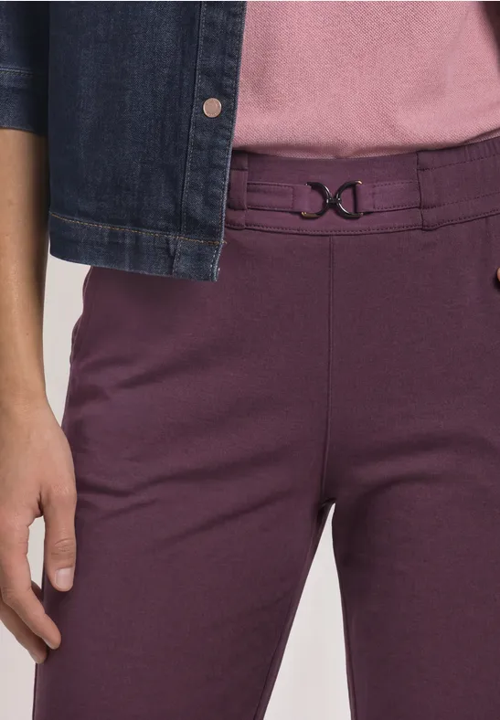 Unterkörper einer Person mit violetten Hosen, dekorativem Bundverschluss und Jeansjacke.