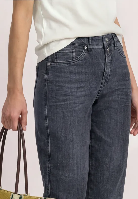Eine Person trägt dunkle High-Waist-Jeans und hält eine braune Handtasche, weißes Oberteil teilweise sichtbar.