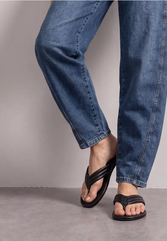 Beine in blauen Jeans und schwarzen Flip-Flops