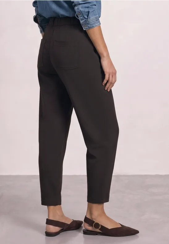Knöchellange, schwarze Hose mit geradem Schnitt, kombiniert mit flachen, braunen Slingback-Schuhen.