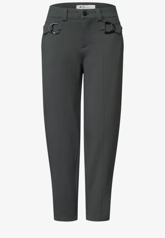 Dunkelgraue, lässige Hose mit leicht zulaufenden Beinen, Gürtelschlaufen und markanten Metallringen an den Taschen.