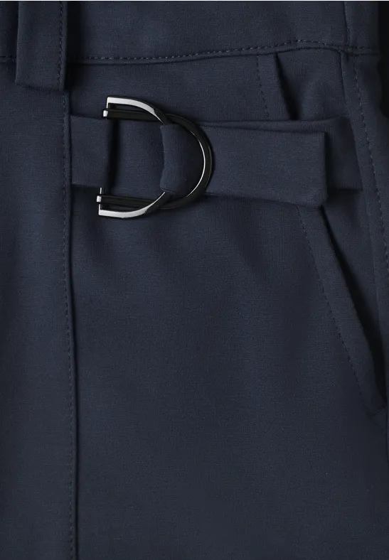 Dunkelblauer Stoff mit silbernem D-Ring an Gürtelband, Detailaufnahme neben einer Tasche.