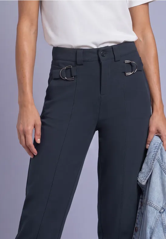 Person trägt weiße Bluse und dunkelblaue, elegante Hose mit D-Ringen am Bund, hält Jeansjacke.