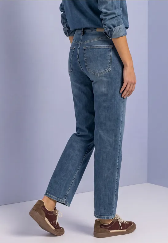 Rückansicht einer Person in blauen Jeans und braunen Schuhen vor einfarbigem Hintergrund.