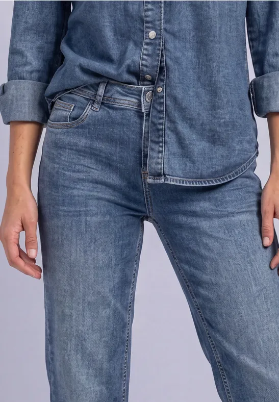 Person trägt dunkelblaues Jeanshemd und Jeanshose, Blick nicht sichtbar, Hände locker an den Seiten.