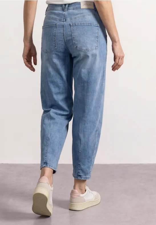 Vrouw van achteren in losse lichtblauwe spijkerbroek en witte sneakers.