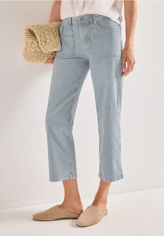 Une personne porte un jean bleu clair court, des mocassins beiges et tient un sac en paille.