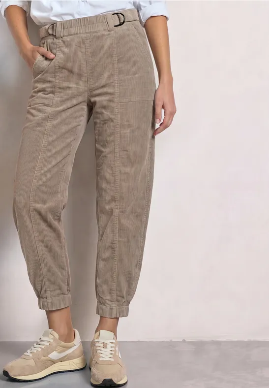 Pantalon beige en velours côtelé, taille et chevilles élastiques, porté avec des baskets claires.