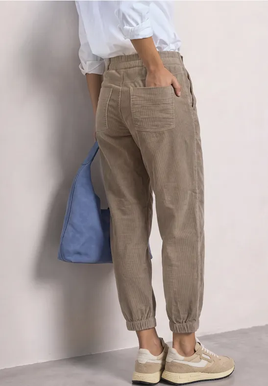 Une personne porte un pantalon en velours beige, des baskets blanches et un sac bleu.