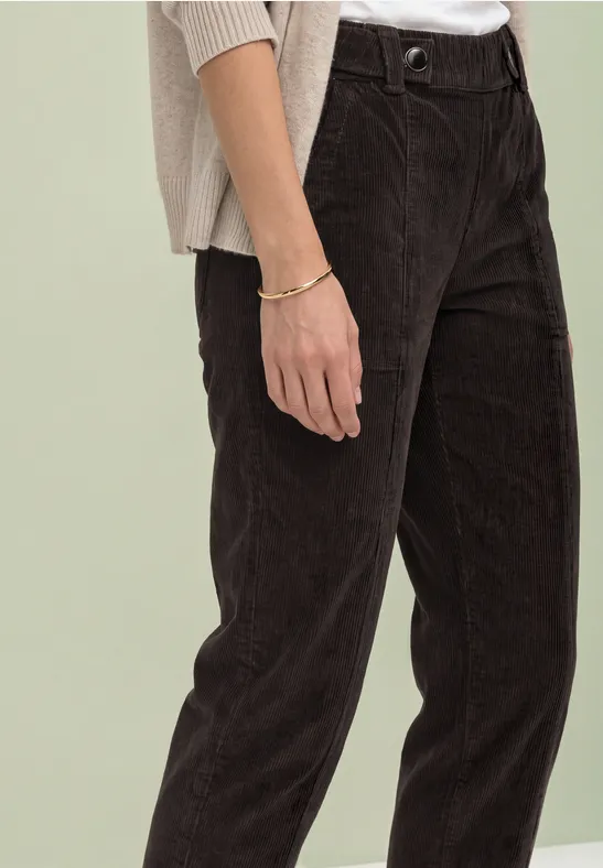 Gedeeltelijk beeld van persoon in donkerbruine corduroy broek, licht topje en zichtbaar armbandje.