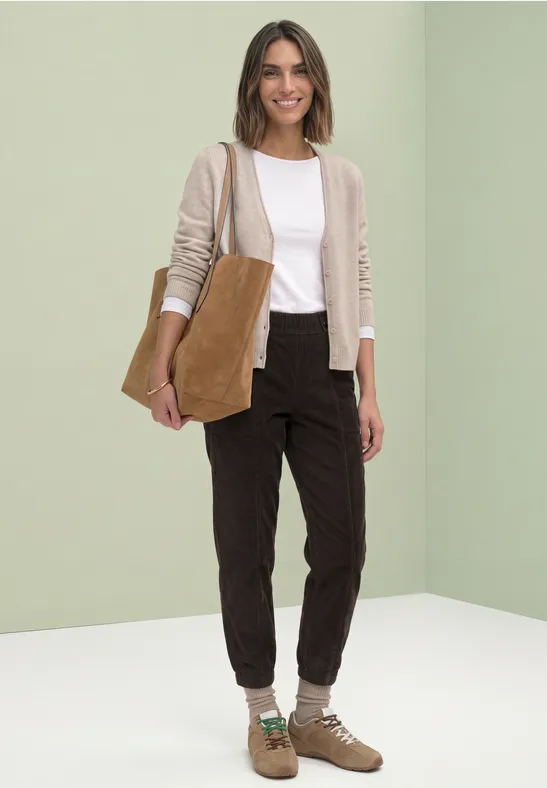 Vrouw met beige vest, wit shirt, donkere broek, bruine enkellaarzen en een bruin schoudertasje.