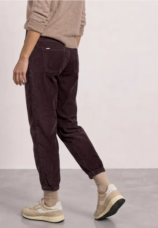 Person steht seitlich, trägt braune Cordhose und beige Sneaker.
