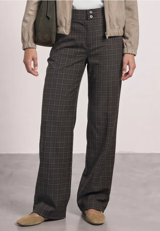 Weite, dunkelgraue Stoffhose mit dezentem Karomuster, kombiniert mit heller Jacke und beigen Slippern.