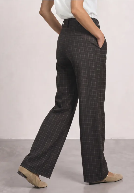 Eine Person trägt weite, braun-karierte Hose mit Taschen und beigen Loafers.