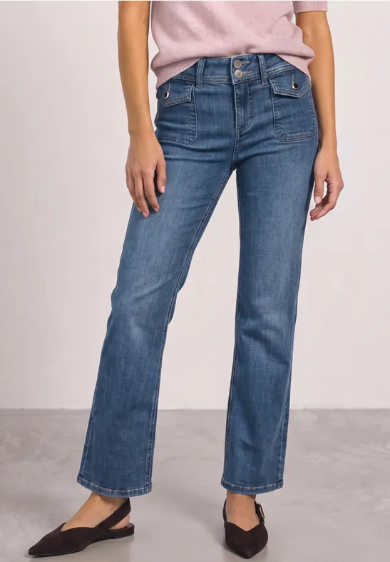 Frau in blauen, gerade geschnittenen Jeans und schwarzen Ballerinas, nur Unterkörper sichtbar.