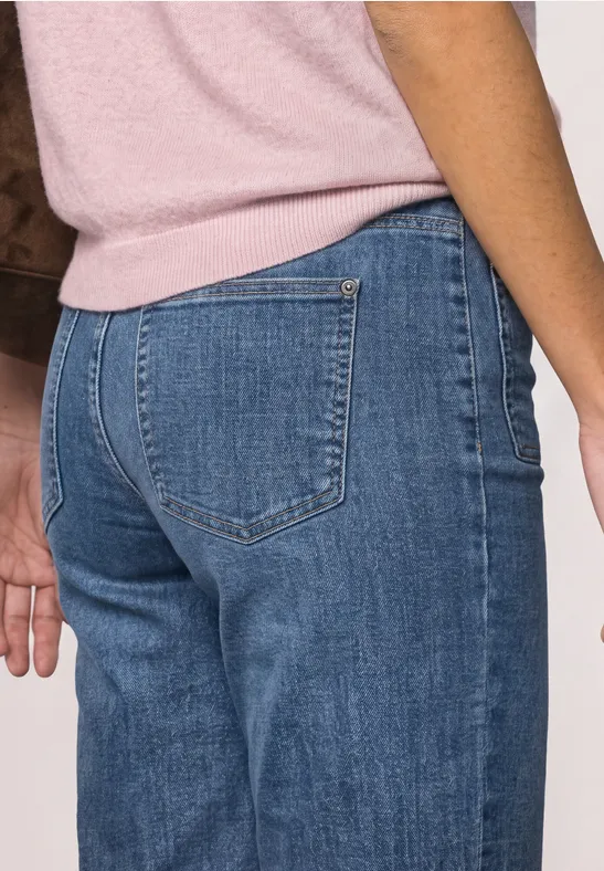 Person von hinten, trägt blaue Jeans und rosa Oberteil.