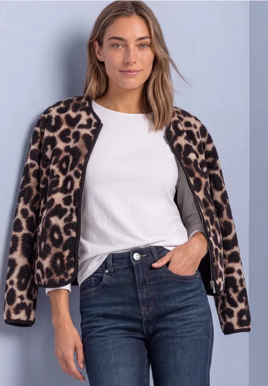 Frau in weißem T-Shirt, Jeans und Leopardenjacke über den Schultern vor neutralem Hintergrund.